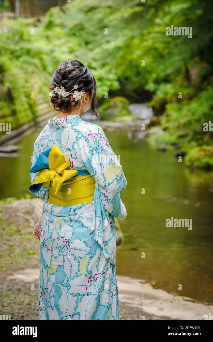 Rückansicht einer Frau mit japanischem Yukata-Sommerkimono, die neben einem Fluss im Kyoto-Naturwald steht. Kyoto, Japan. Stockfoto
