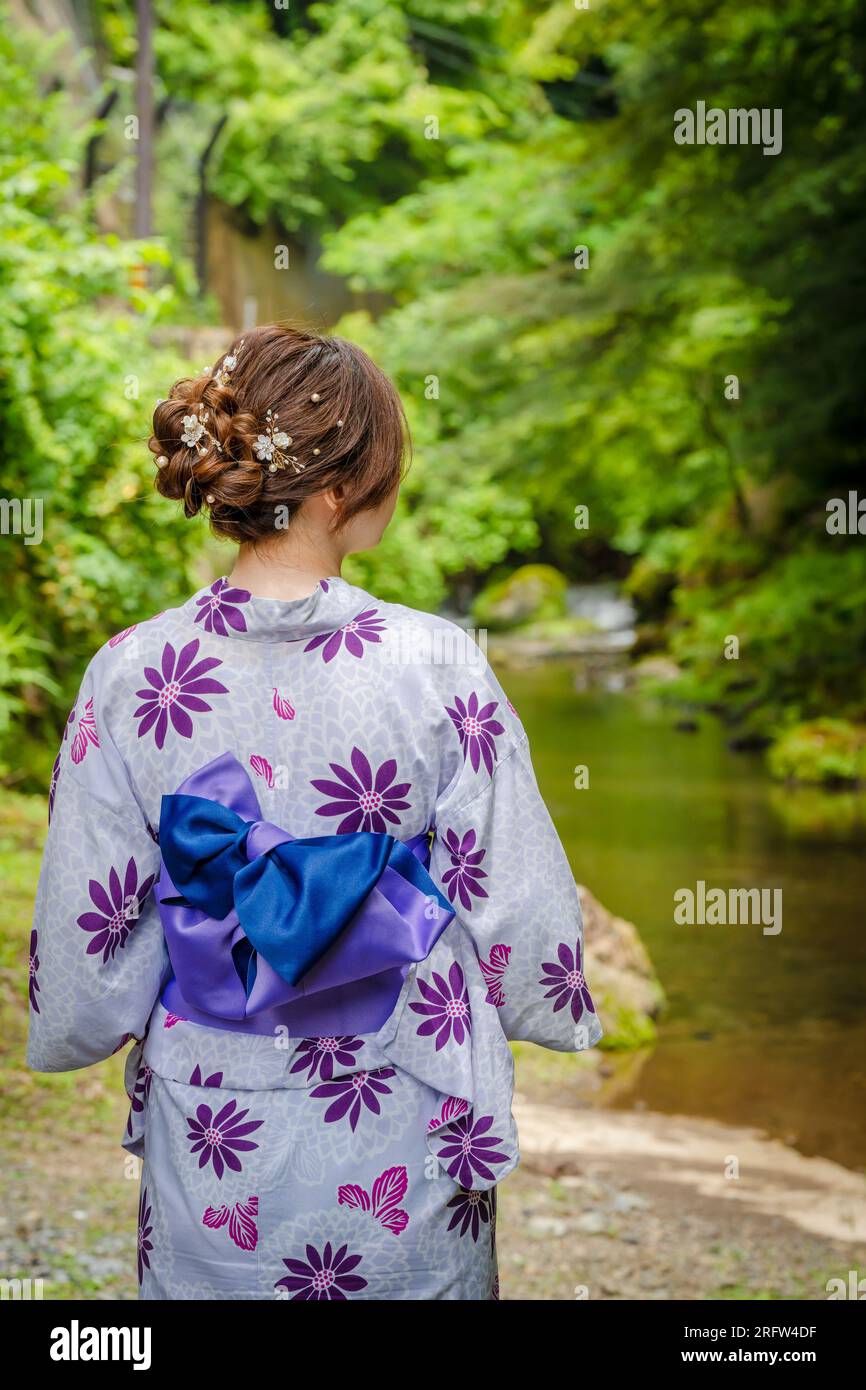 Rückansicht einer Frau mit japanischem Yukata-Sommerkimono, die neben einem Fluss im Kyoto-Naturwald steht. Kyoto, Japan. Stockfoto