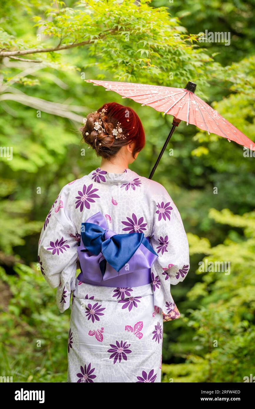Rückansicht einer Frau, die einen japanischen Yukata-Sommerkimono trägt und einen traditionellen japanischen Ölpapierschirm im Naturwald hält. Kyoto, Japan. Stockfoto