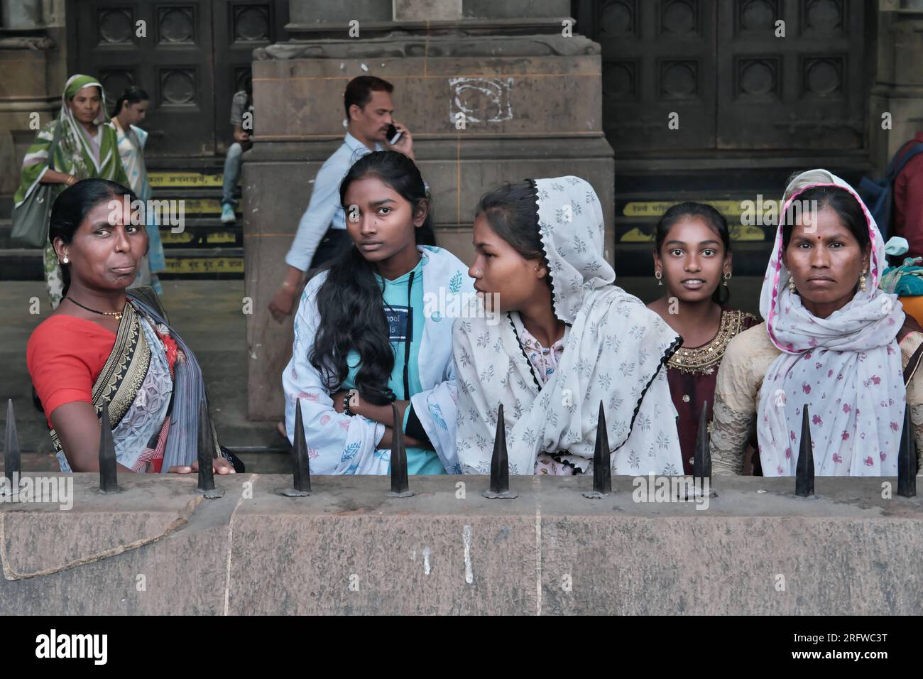 Eine Gruppe von fünf Frauen, jung und alt, steht vor dem Chhatrapati Shivaji Maharaj Terminus (CSMT) in Mumbai, Indien, und schaut sternd in die Kamera Stockfoto