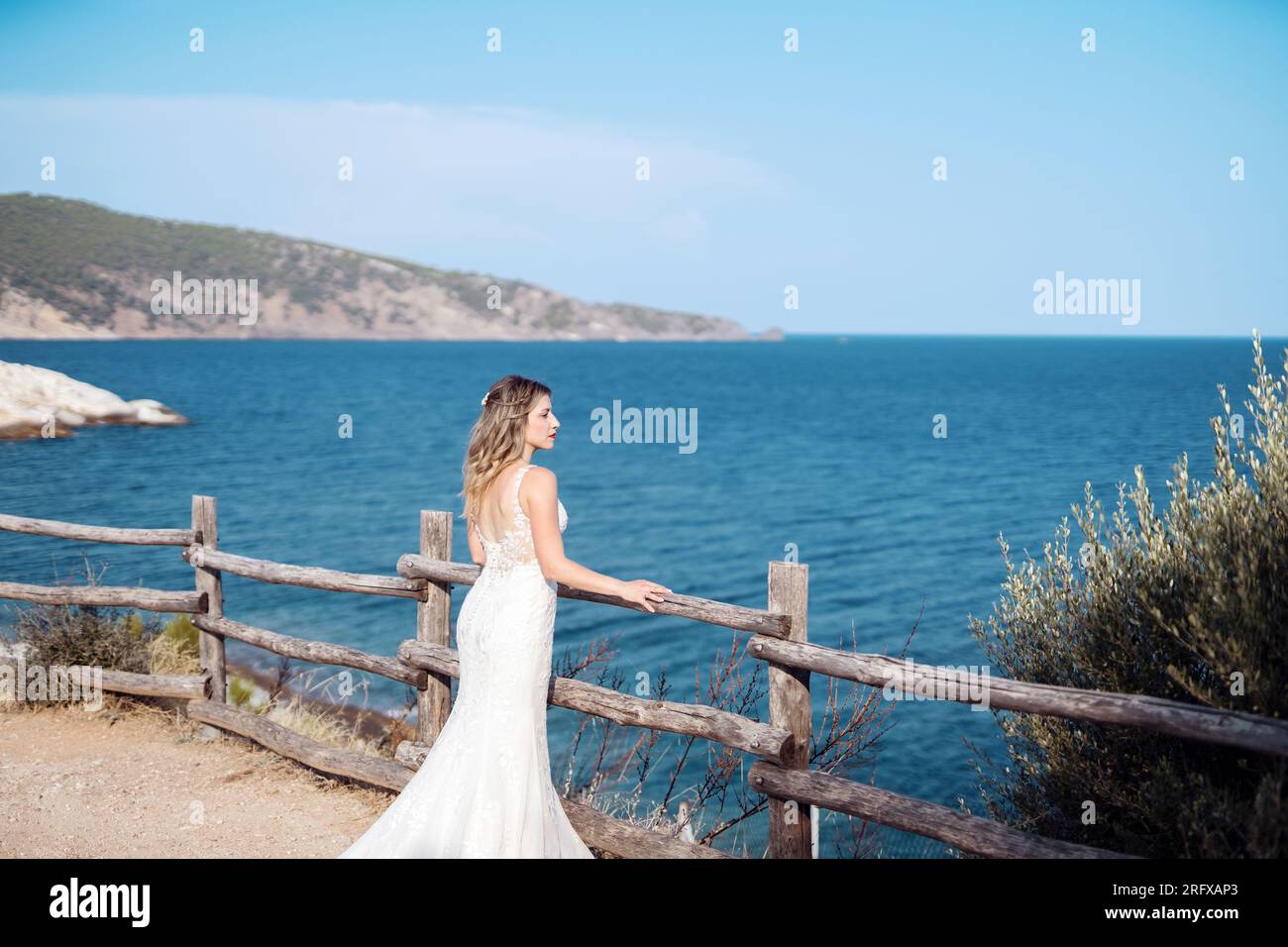 Eine wunderschöne Braut mit einem traumhaften Kleid, blickt auf das Meer. Stockfoto