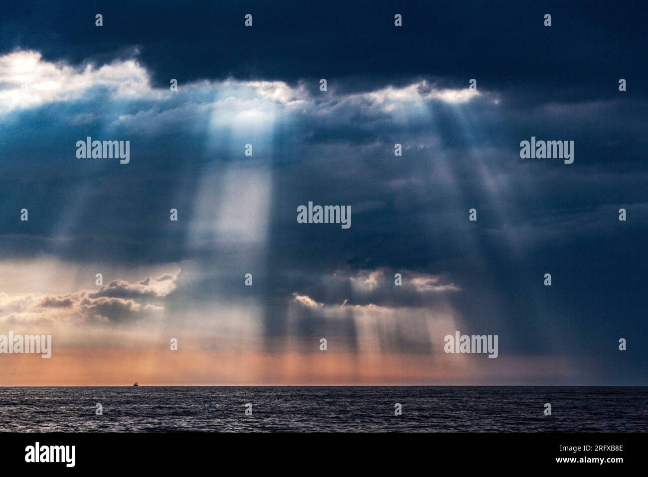 Die Sonne bricht durch die Wolken und erhellt das Meer mit seinen Strahlen Stockfoto