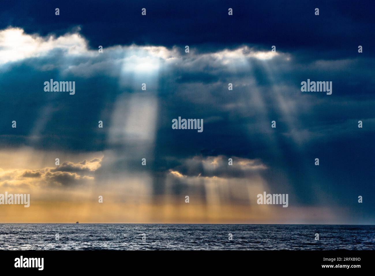 Die Sonne bricht durch die Wolken und erhellt das Meer mit seinen Strahlen Stockfoto