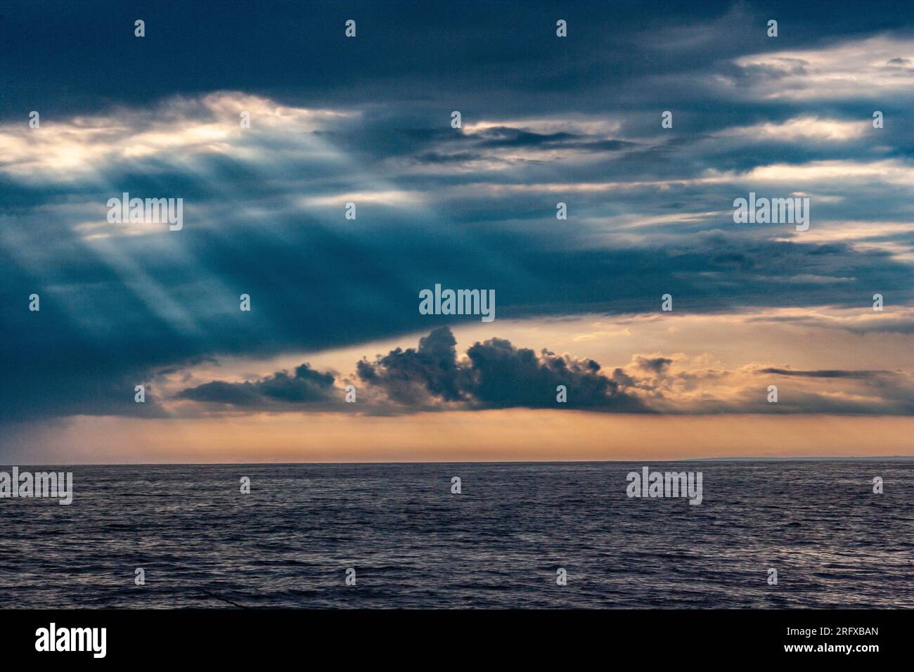 Die Sonne bricht durch die Wolken und erhellt das Meer mit seinen Strahlen Stockfoto