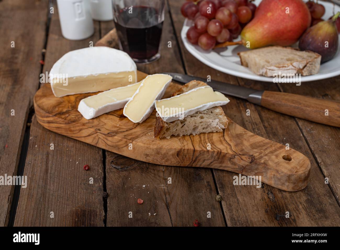 Camembertkäse in Scheiben auf Brotstück mit Früchten und einem Glas Wein im Hintergrund Stockfoto