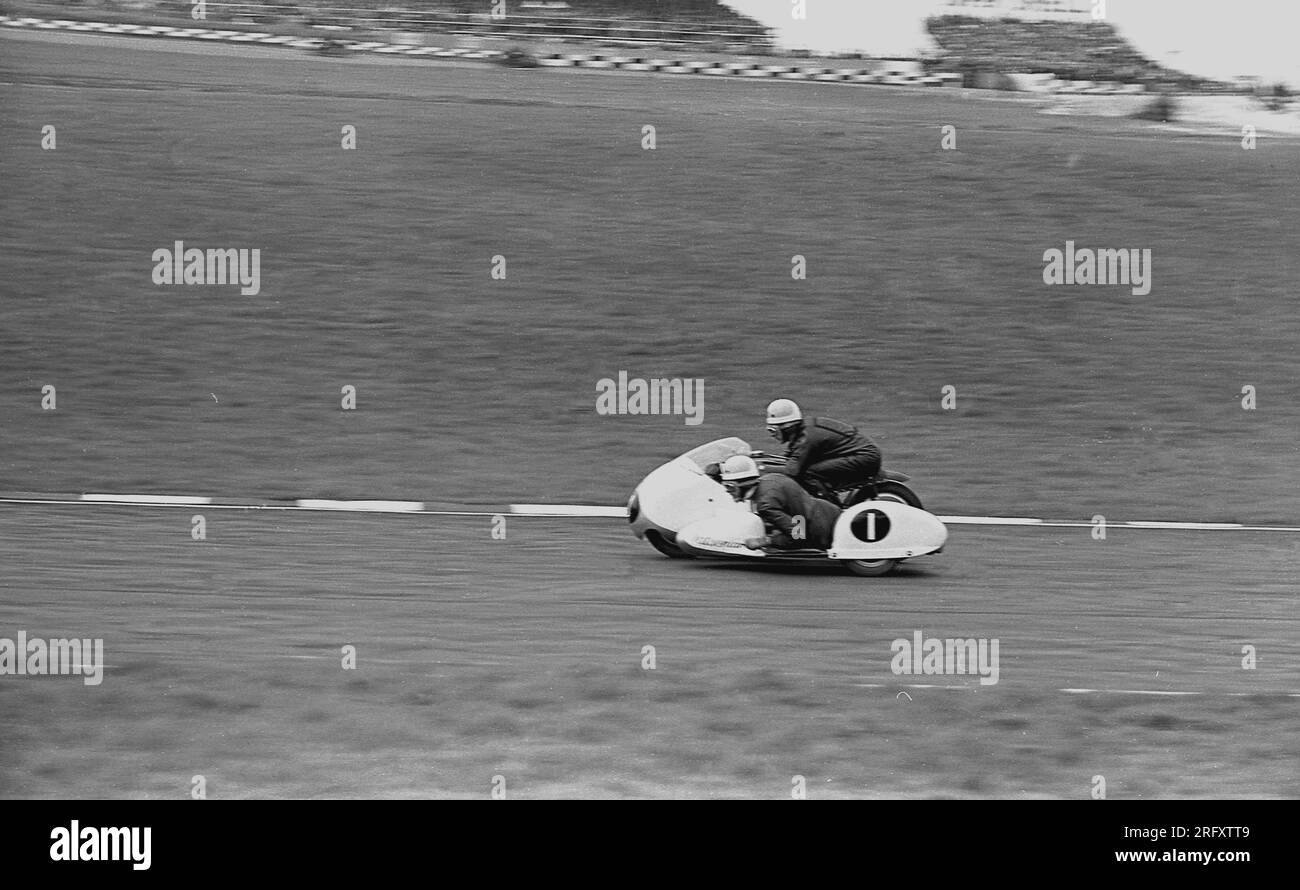 1960er, historisch, Sidecar-Rennen aus dieser Zeit, ein Motorrad mit Beiwagen, ein 3-rädriges Motorrad draußen auf einer Rennstrecke, England, Großbritannien. Beim Fahren mit hoher Geschwindigkeit durch Kurven ist das Sidecar Racing die einzige Form des Motorsports, bei der Beifahrer und Fahrer das Fahrzeug steuern und erstmals in den frühen 1920er Jahren bei den TT-Rennen auf der Isle of man gesehen wurden. Stockfoto