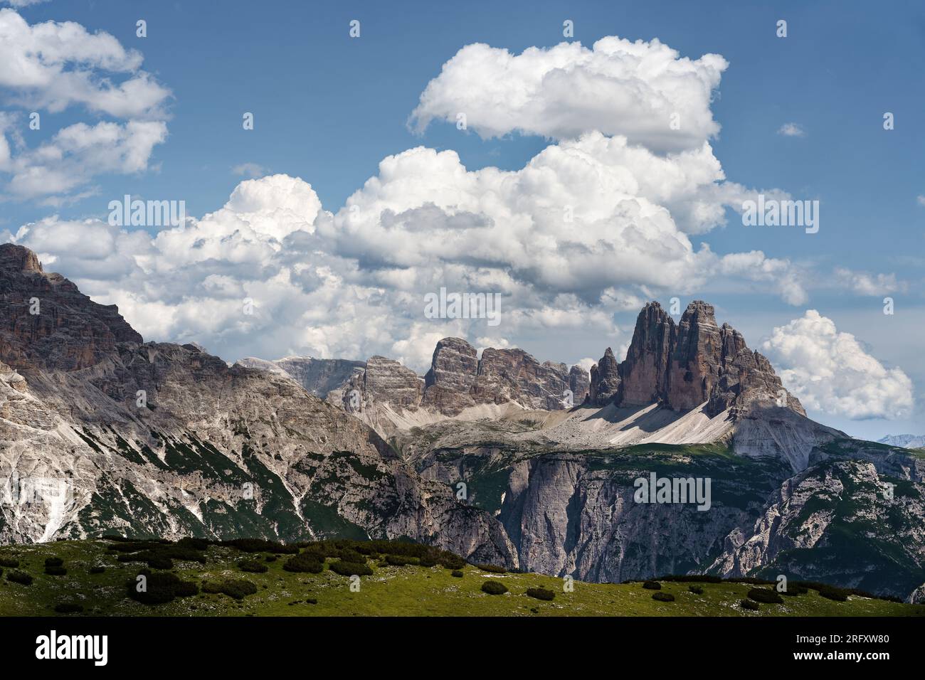 Blick auf die berühmte Felsformation drei Zinnen und ihre Umgebung aus der Ferne, blauer Himmel mit imposanten Wolkenformationen mit teilweisen Schatten Stockfoto