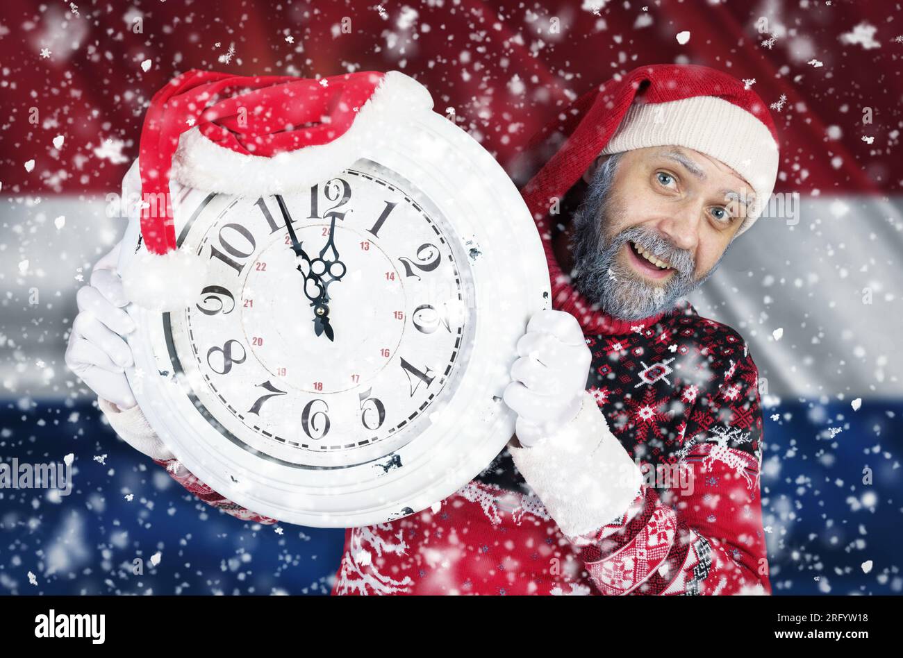 Der Weihnachtsmann hält eine Uhr in der Hand, an der vor dem Hintergrund der niederländischen Flagge noch 5 Minuten bis zum Neujahr, Weihnachten, verbleiben. Stockfoto