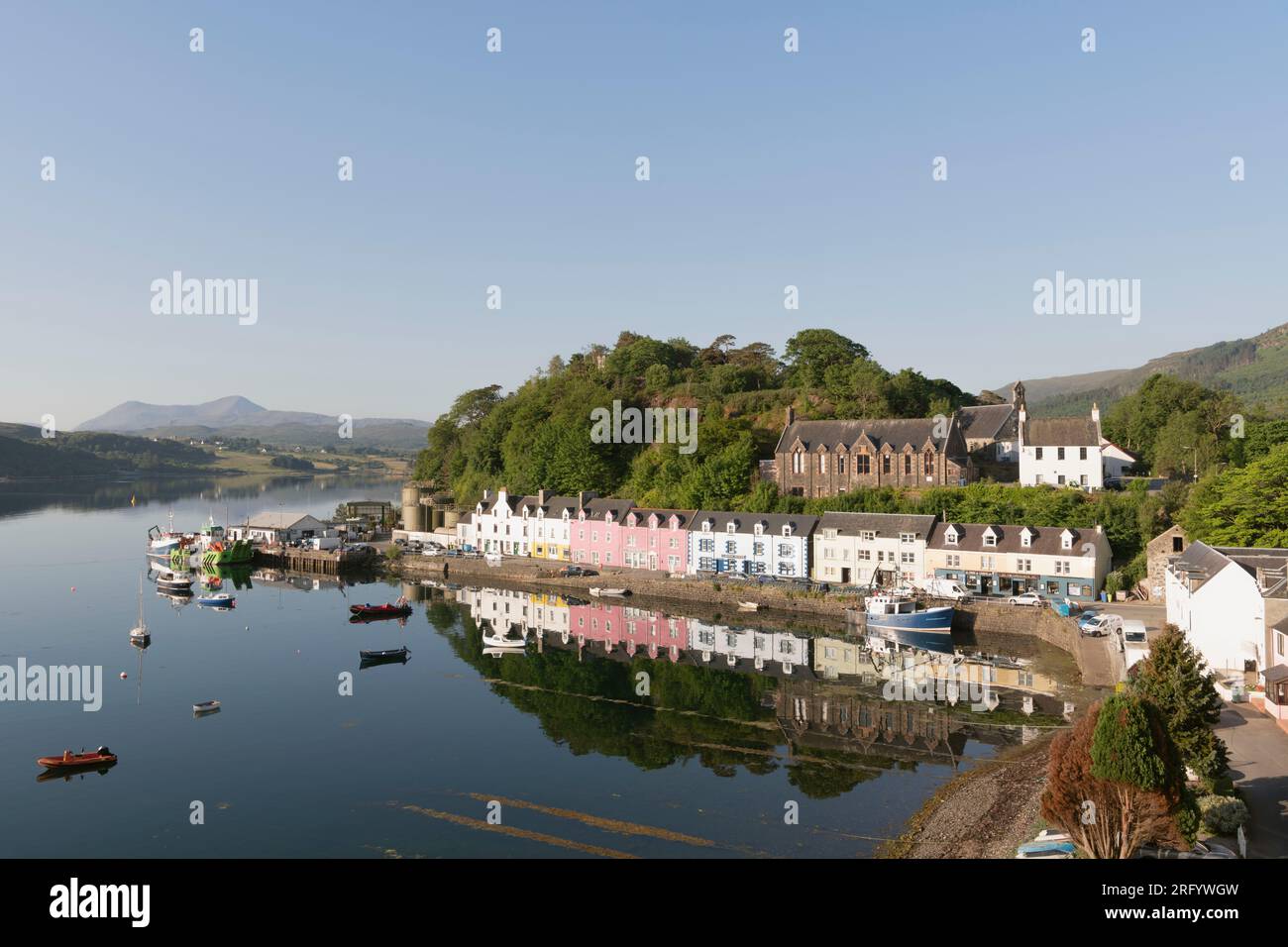 Der Klumpen und die bunten Gebäude in der Quay Street in Portree auf der Isle of Skye spiegeln sich an einem ruhigen Sommermorgen in Loch Portree wider Stockfoto