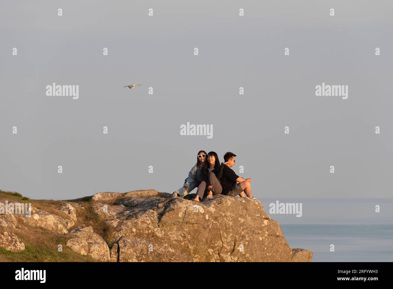 Ein Mann fliegt eine Drohne und fotografiert zwei Frauen, die im Sommer in der späten Abendsonne auf einem Felsvorsprung in der Nähe von Neist Point (Isle of Skye) posieren Stockfoto
