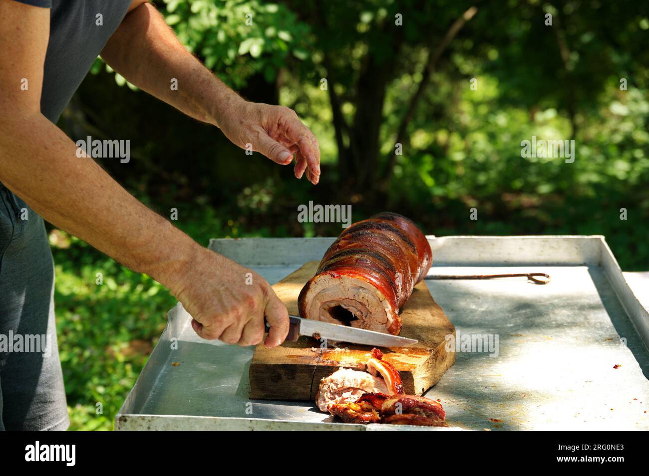Ein kurzer Schuss Hände, der in der Natur großes Stück Schweinefleisch auf den Tisch schneidet Stockfoto