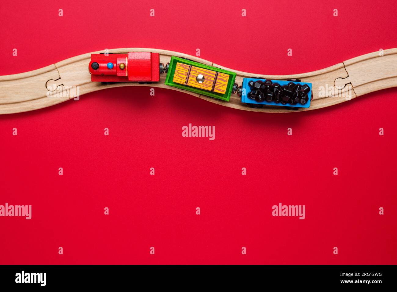Spielzeugzug mit gebogenen Holzschienen auf rotem Hintergrund. Holzlokomotive. Stockfoto