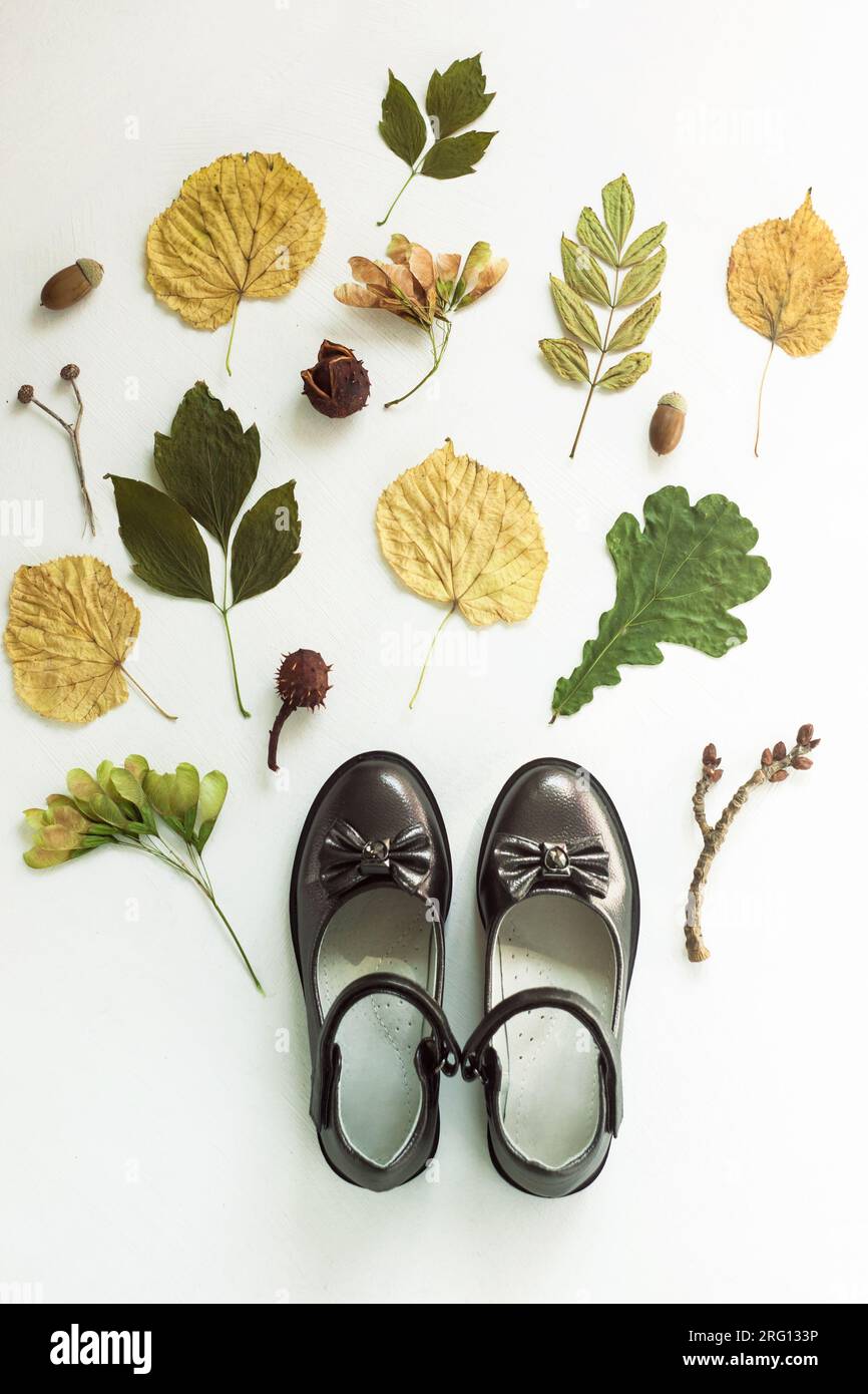 Schwarze Kinderstiefel im Herbstlaub auf weißem Hintergrund, Draufsicht. Schuluniform Schuhe für Mädchen. Herbstflair mit bunten Blättern. Regnerischer Tag, kalt Stockfoto