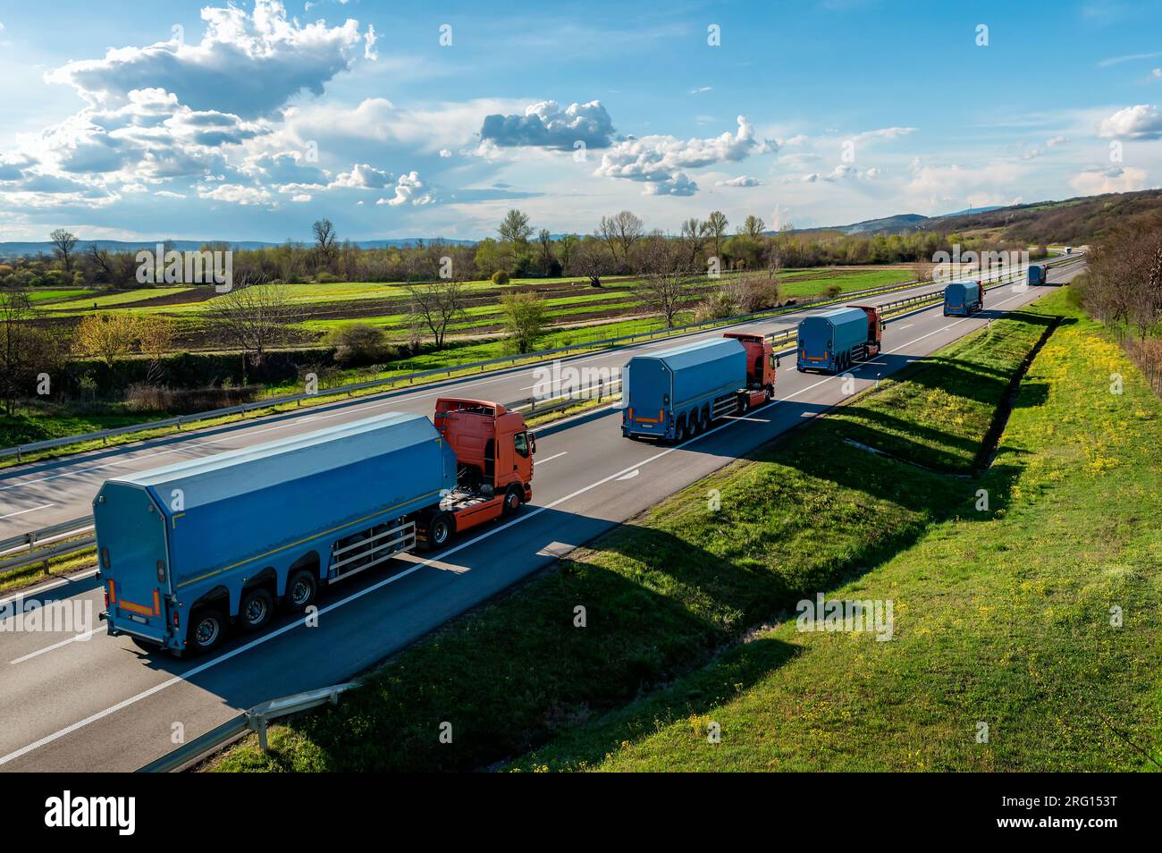 Konvoi oder Fuhrpark von Container-Aufliegern auf einer Autobahn durch eine wunderschöne Landschaft. Multifunktionale Einlage für den Transport von Glas Stockfoto