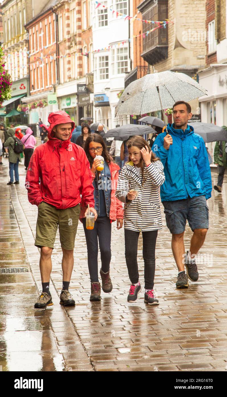 Menschen, die im Regen unter Schirmen in der Hauptstraße Winchester spazieren gehen und einkaufen, während des schrecklichen nassen Sommerwetters in England im Jahr 2023 Stockfoto