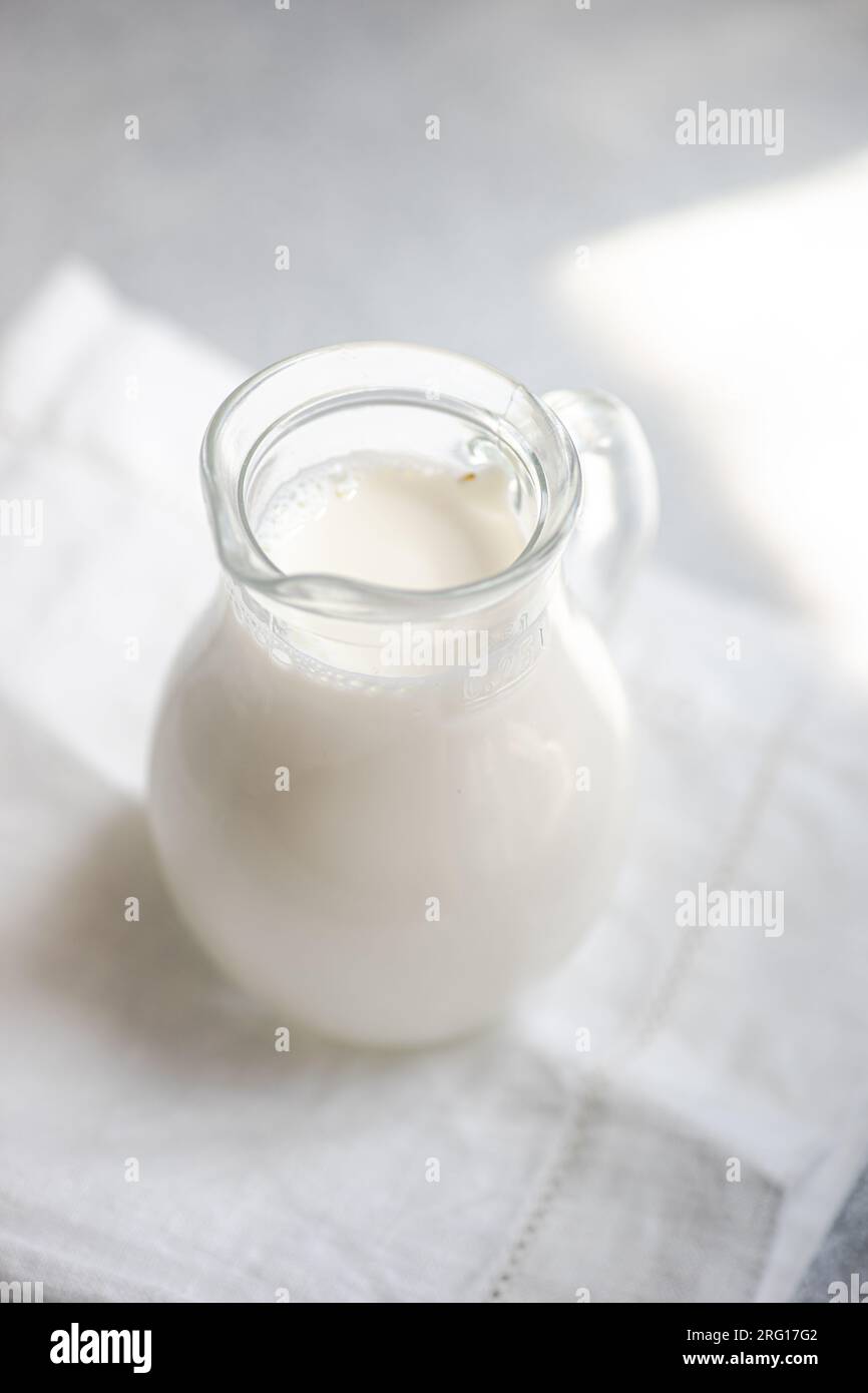 Hoher Winkel von weißer roher Kuhmilch in einem Glasgefäß auf einer weißen Serviette vor verschwommenem Hintergrund Stockfoto