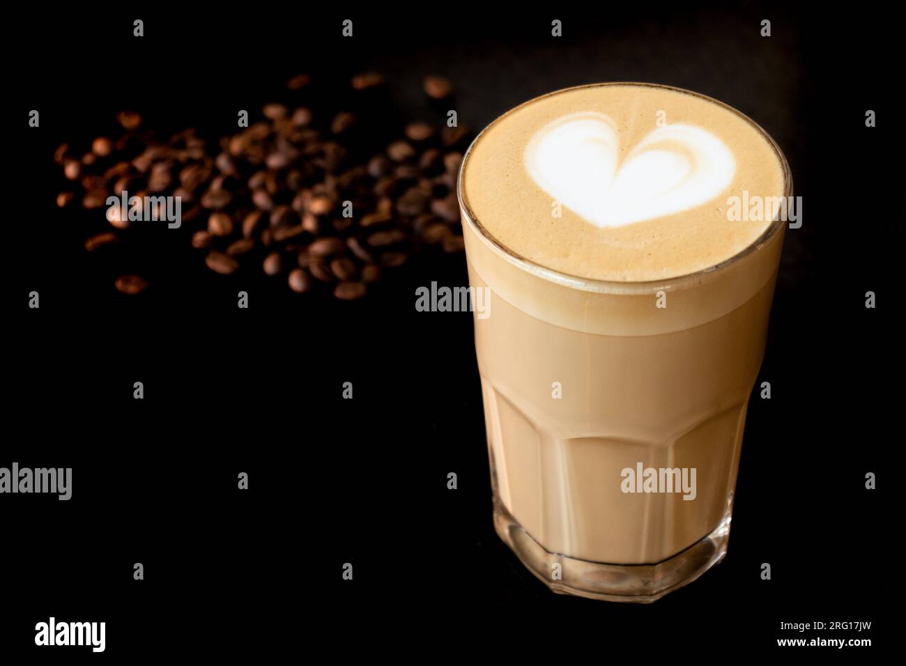 Ein Glas aromatischer, heißer Latte-Kaffee, dekoriert mit Latte Art, auf einem Tisch neben einigen Kaffeebohnen Stockfoto