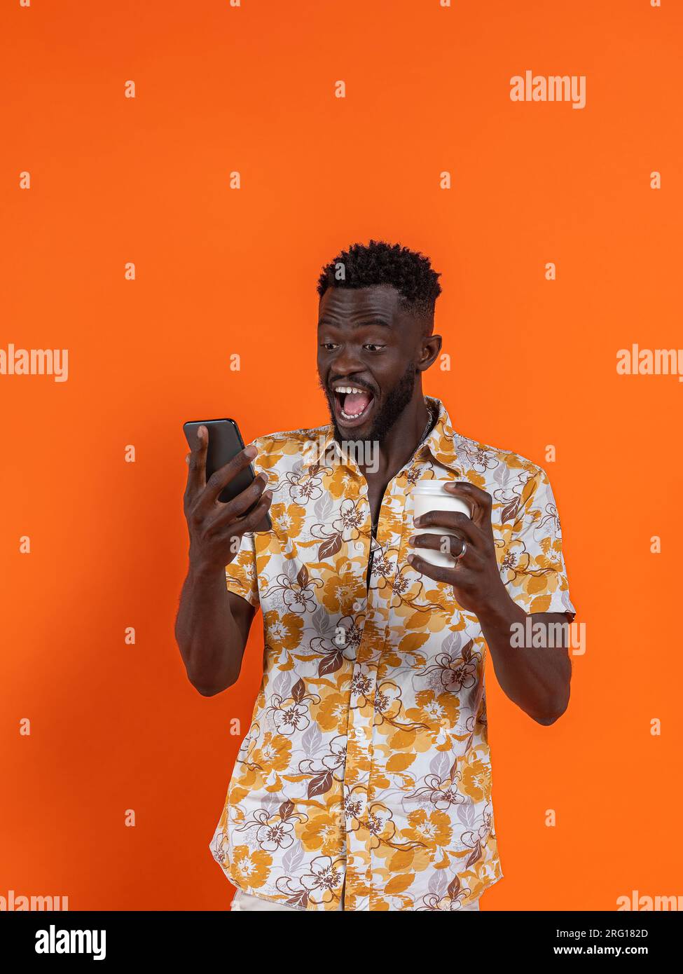 Fröhlicher afroamerikanischer Mann mit Smartphone und Selbstporträt, während er Kartonglas auf orangefarbenem Hintergrund hält Stockfoto