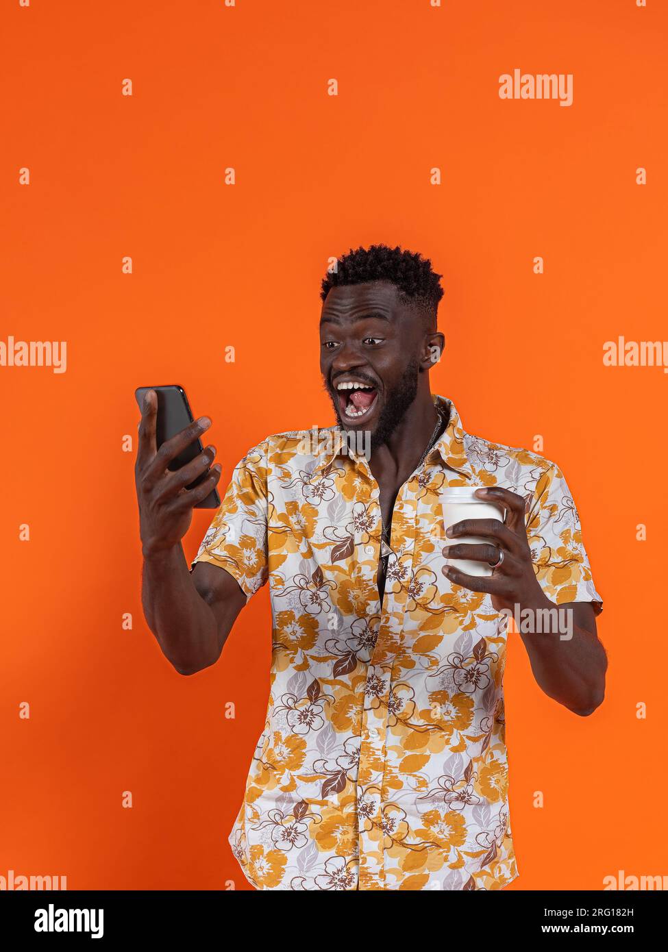 Fröhlicher afroamerikanischer Mann mit Smartphone und Selbstporträt, während er Kartonglas auf orangefarbenem Hintergrund hält Stockfoto