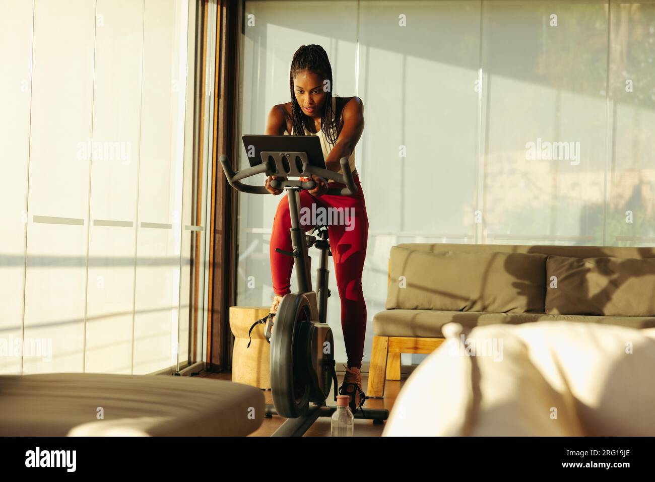Schwarze Frau erreicht ihre Fitnessziele mit Hilfe eines Online-Radkurses. Mit ihrem Tablet vor sich folgt sie dem virtuellen Stockfoto