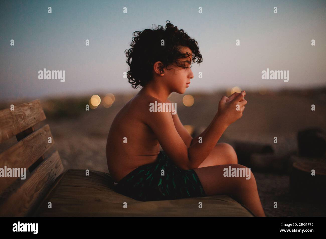 Ein kleiner Junge, der mit seinem Smartphone in der Wüste während des Sonnenuntergangs spielt Stockfoto