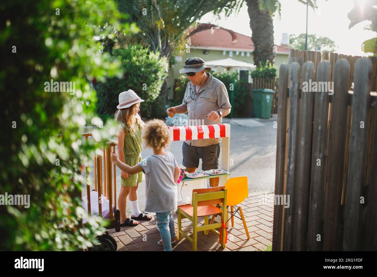 Zwei Schwestern, die mit dem Marktstand spielen und einem vorbeigehenden Mann Waren verkaufen Stockfoto