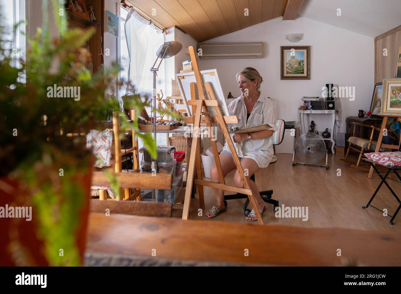 Ein Blick auf eine reife Malerin, die ein Gemälde in ihrem Atelier kreiert. Stockfoto
