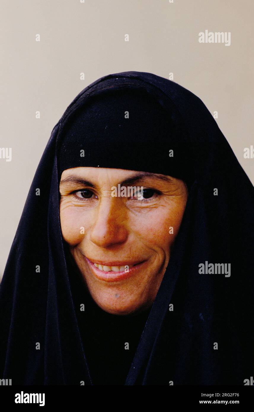 Irakisches Porträt einer Frau mit Hijab, der allgemeine arabische Begriff für bescheidene Kopfbedeckung. Es besteht aus zwei Teilen, dem Schal im Al-Amira-Stil, und das eng anliegende, elastische schwarze Band, das auf ihrer Stirn sichtbar ist, ist ein Untertuch. Sie hält ihr Haar fern und bietet eine sichere Basis für die äußere Schicht. Die Abaya: Der äußere schwarze Stoff ist tatsächlich der obere Teil ihrer Abaya, der über ihrem Kopf hängt. Im traditionellen irakischen Stil ist die Abaya nicht nur ein Mantel für die Schultern, sie beginnt von der Kopfkrone und fließt bis zu den Füßen. Marsh Arabische Frau lebt in Bagdad Irak 1980er Jahre 1984. Stockfoto