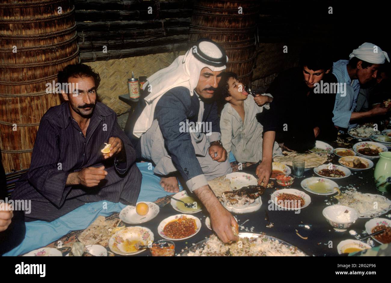 Marsh Arabs Southern Iraq 1984. Das Bankett findet in einem traditionellen Reed-Gebäude statt, das als Mudhif bezeichnet wird. Nur männliche Mitglieder der Gemeinde waren anwesend. Sie essen - nehmen Sie das Essen mit der linken Hand. Hammar marschiert im Irak 1980er HOMER SYKES Stockfoto