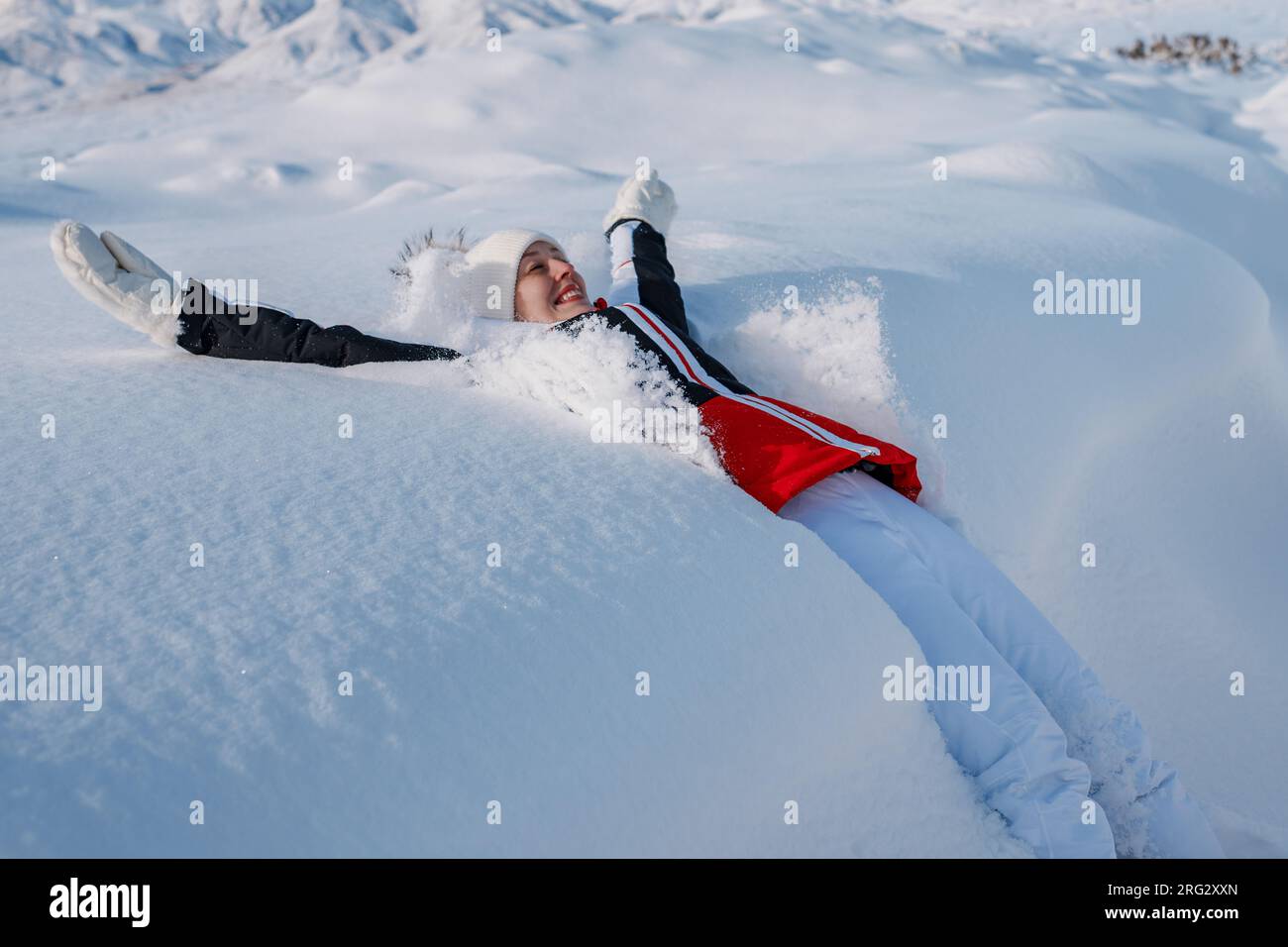 Junge, fröhliche Touristin, die im Winter in den Schnee fällt Stockfoto