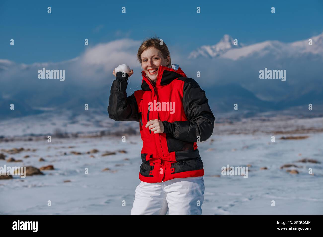 Eine junge Frau wirft einen Schneeball auf den Berghintergrund Stockfoto