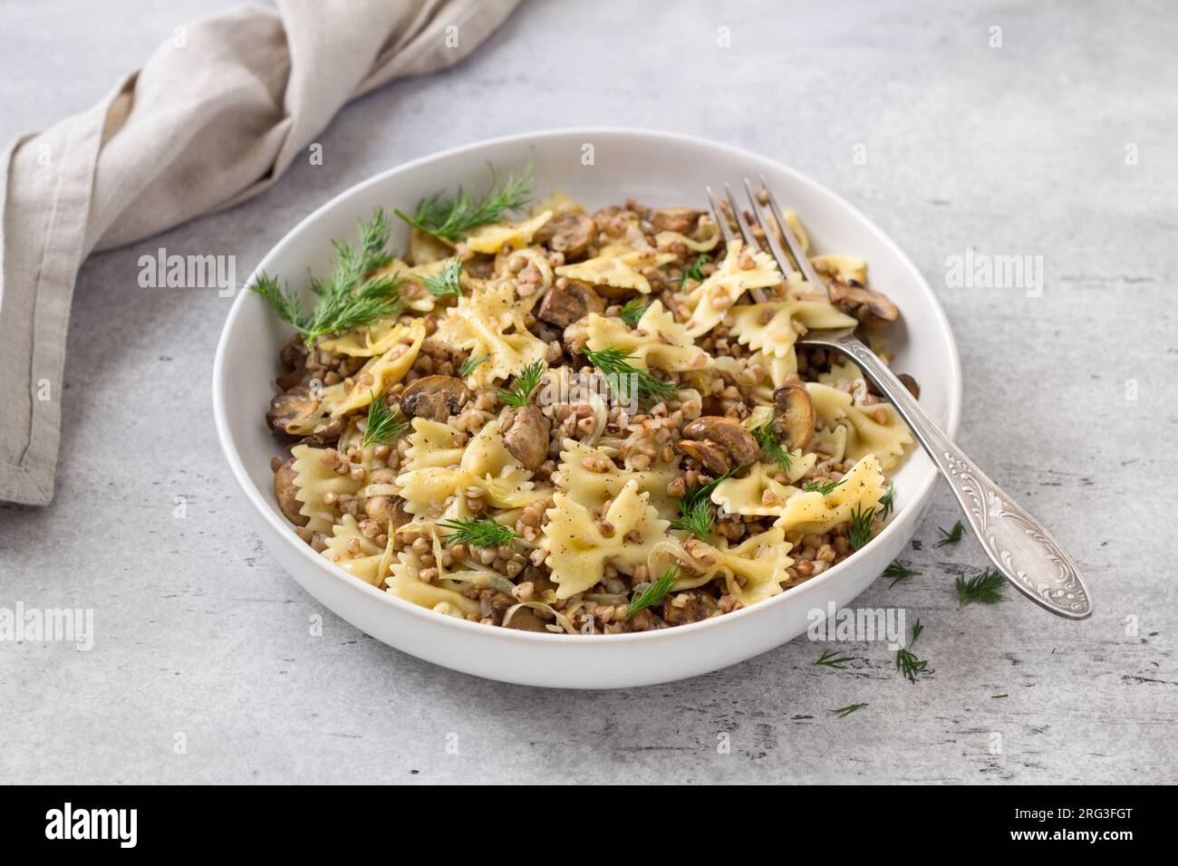 Traditionelles jüdisches Gericht Kasha Varnishkes: Buchweizen, Pasta, Champignon-Pilze, gebratene Zwiebeln mit Kräutern auf grauem, strukturiertem Hintergrund, vegane Speisen, t Stockfoto