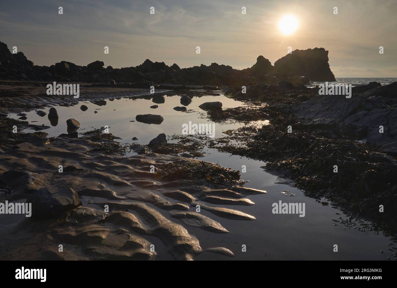 Sonnenuntergang über einem Ufer bei Ebbe, mit gewelltem Sand, einem Felsenpool und Felsen, am Hartland Quay, Hartland, Atlantikküste von Devon, Großbritannien. Stockfoto
