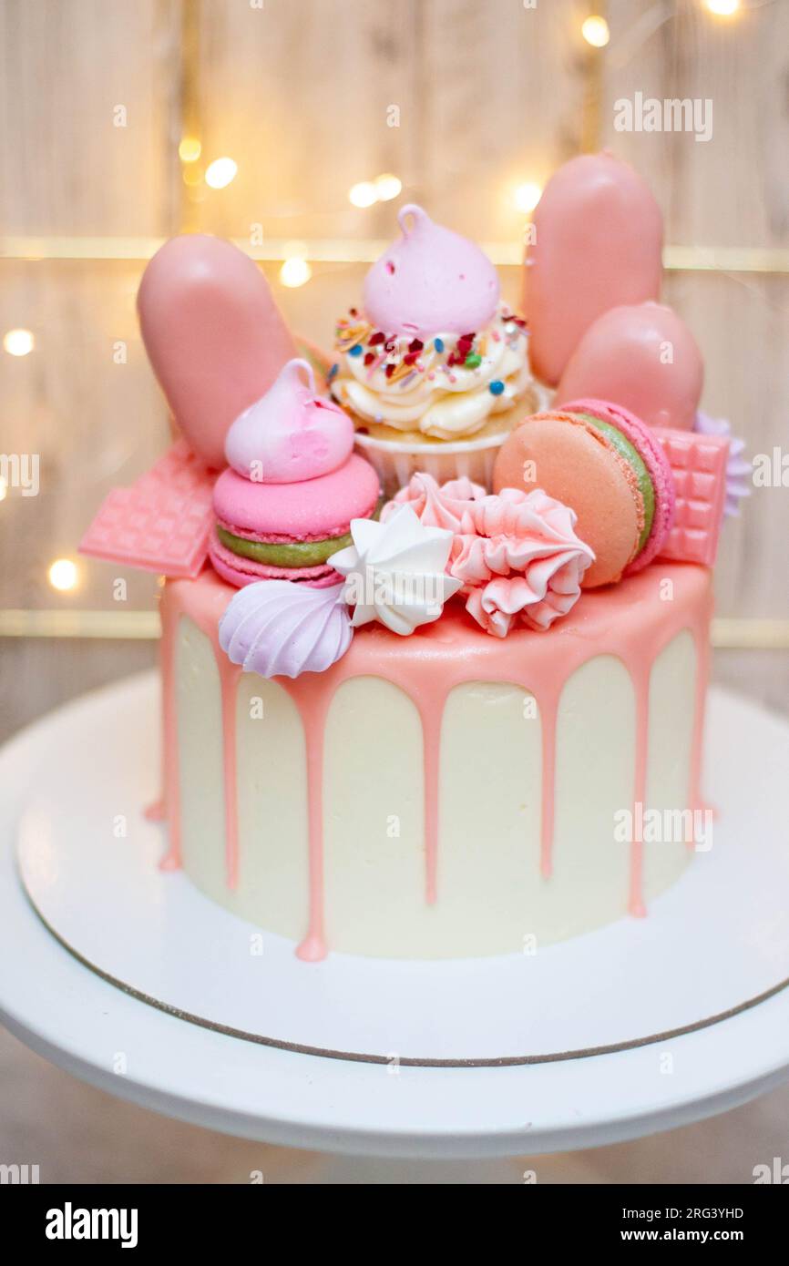 Wunderschöner Kuchen dekoriert mit geschmolzener rosa Schokolade, Makronen, Baiser, Kuchenpops und Süßigkeiten auf festlichem Hintergrund Stockfoto