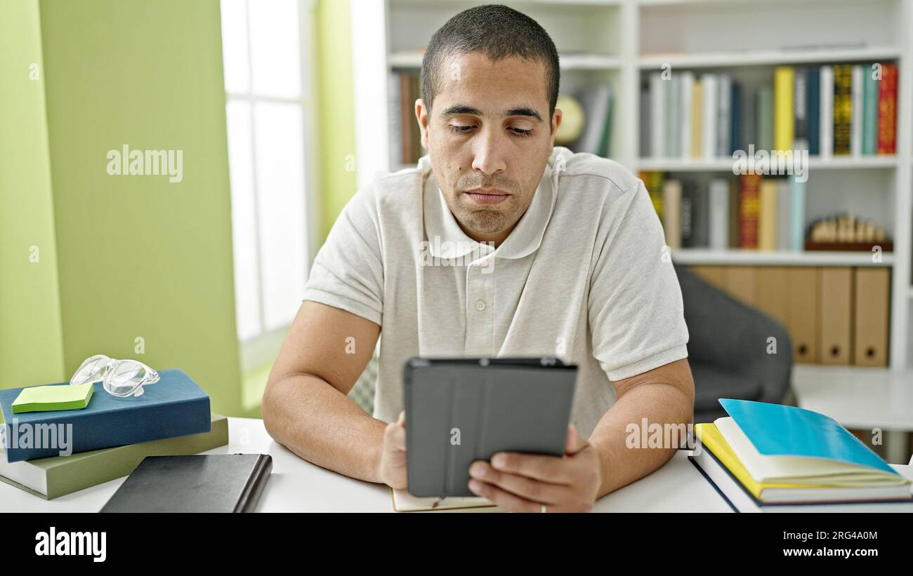 Junger hispanischer Student, der Touchpad benutzt und an der Bibliotheksuniversität studiert Stockfoto