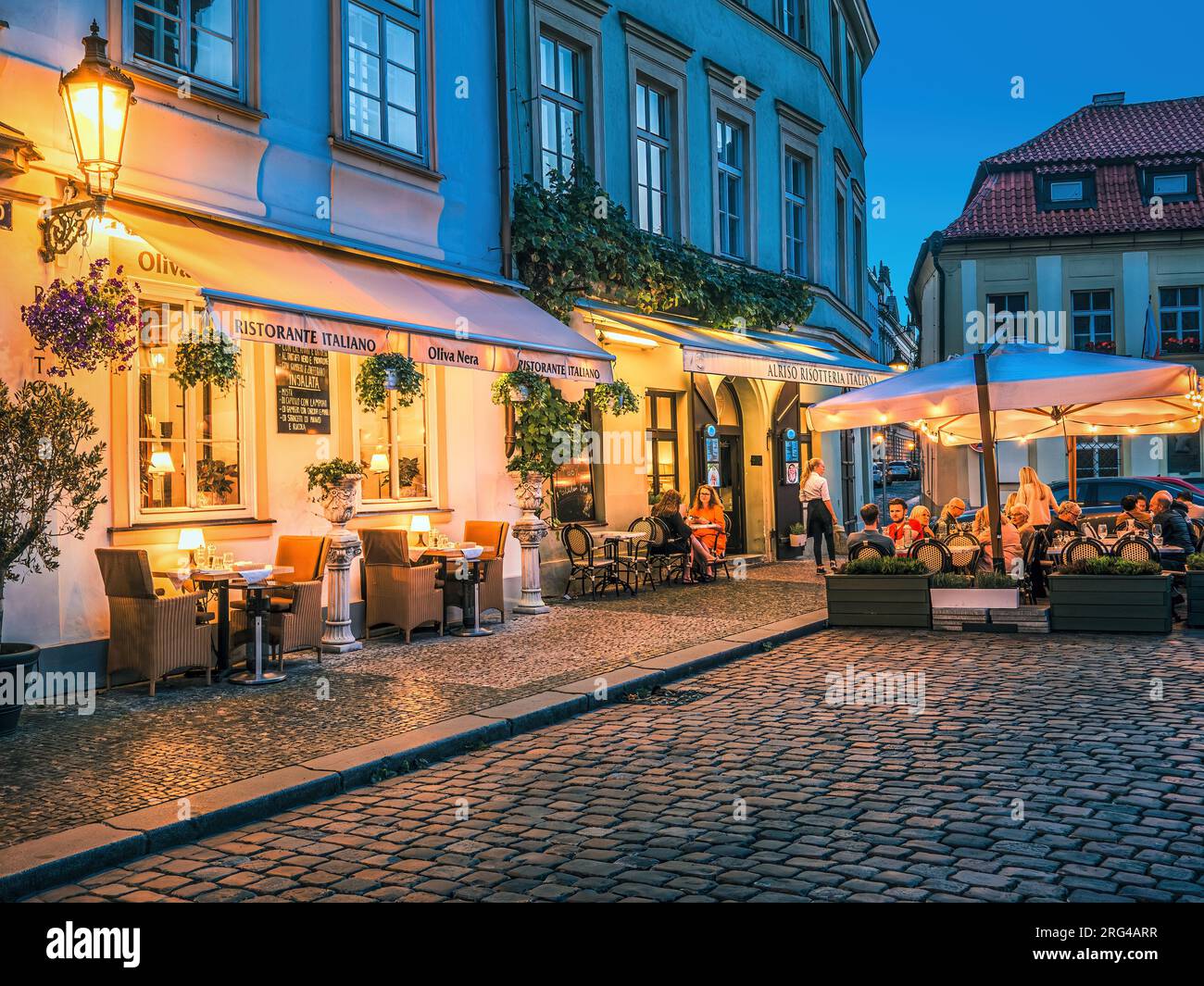 Gäste sitzen in einem beleuchteten italienischen Restaurant im Freien in der kleinen Kopfsteinpflasterstraße der Prager Altstadt. Stockfoto