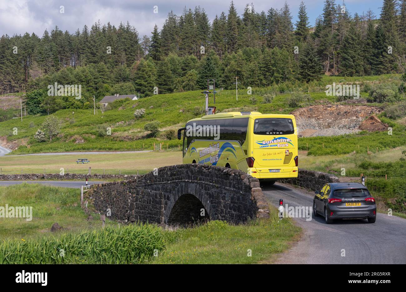 Isle of Mull, Schottland, Vereinigtes Königreich. 6. Juni 2023 Der Tourbus fährt über eine kleine, schmale Buckelbrücke auf der A849. Straße, Isle of Mull, Schottland. Stockfoto