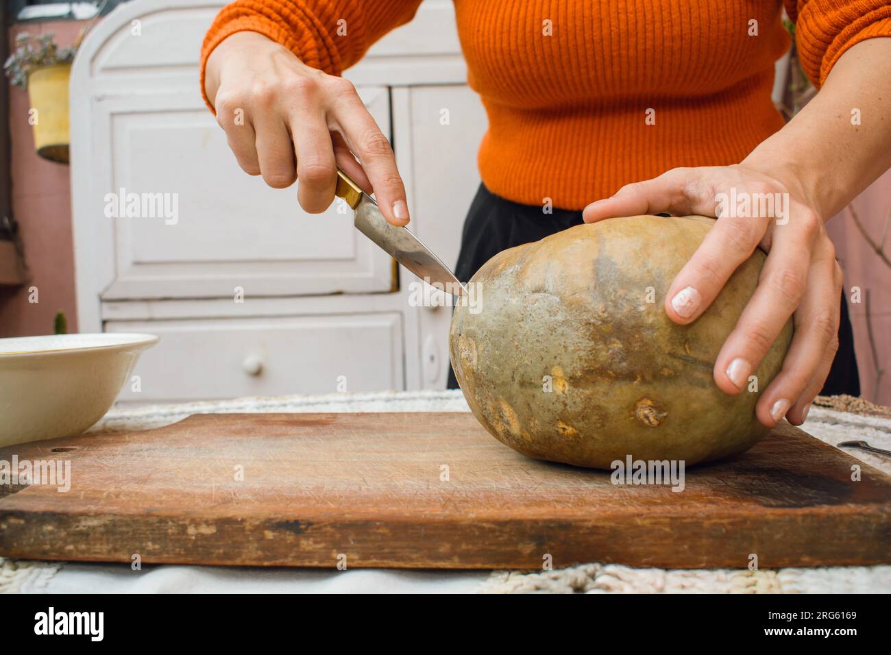 Eine unbekannte Frau zu Hause, die Hallooween einen Kürbis auf einen Tisch schneidet, mit einem Messer, Vorderansicht, Kopierraum. Stockfoto