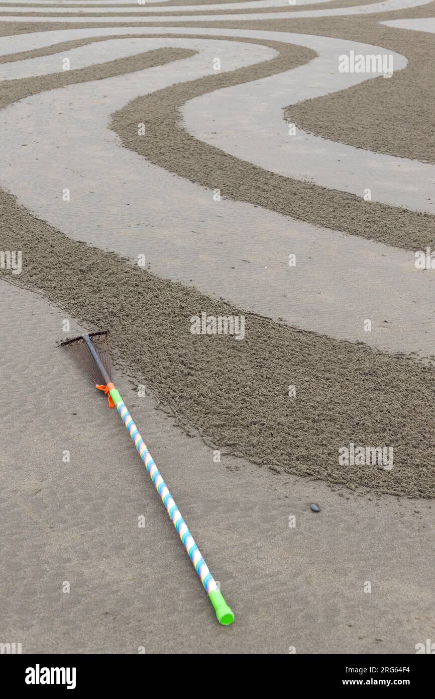 Ein Rechen auf dem Boden neben einem Sandlabyrinth, das von Circles in the Sand in Bandon, Oregon, geschaffen wurde. Stockfoto