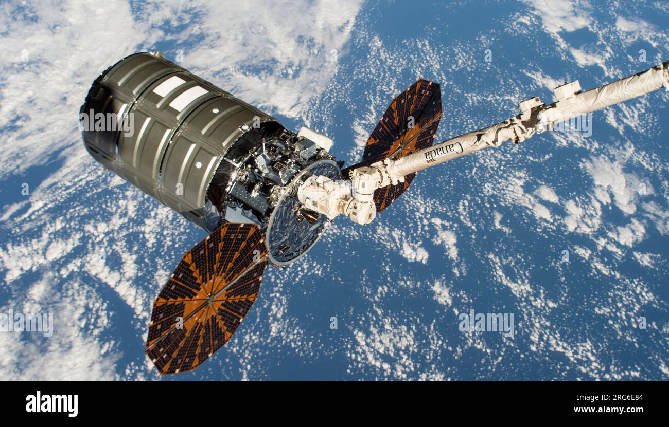 Das Cygnus-Frachtraum ist in den Griffen des Canadarm2 Roboterarms über der Erde abgebildet. Stockfoto