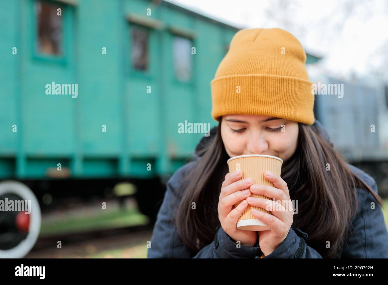Kaffeepause im Bahnhofsgebäude: Junge Latina in warmer Kleidung, die eine Tasse Kaffee zum Mitnehmen isst. Speicherplatz kopieren Stockfoto