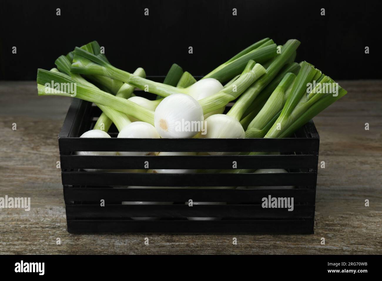 Schwarze Kiste mit grünen Frühlingszwiebeln auf Holztisch Stockfoto