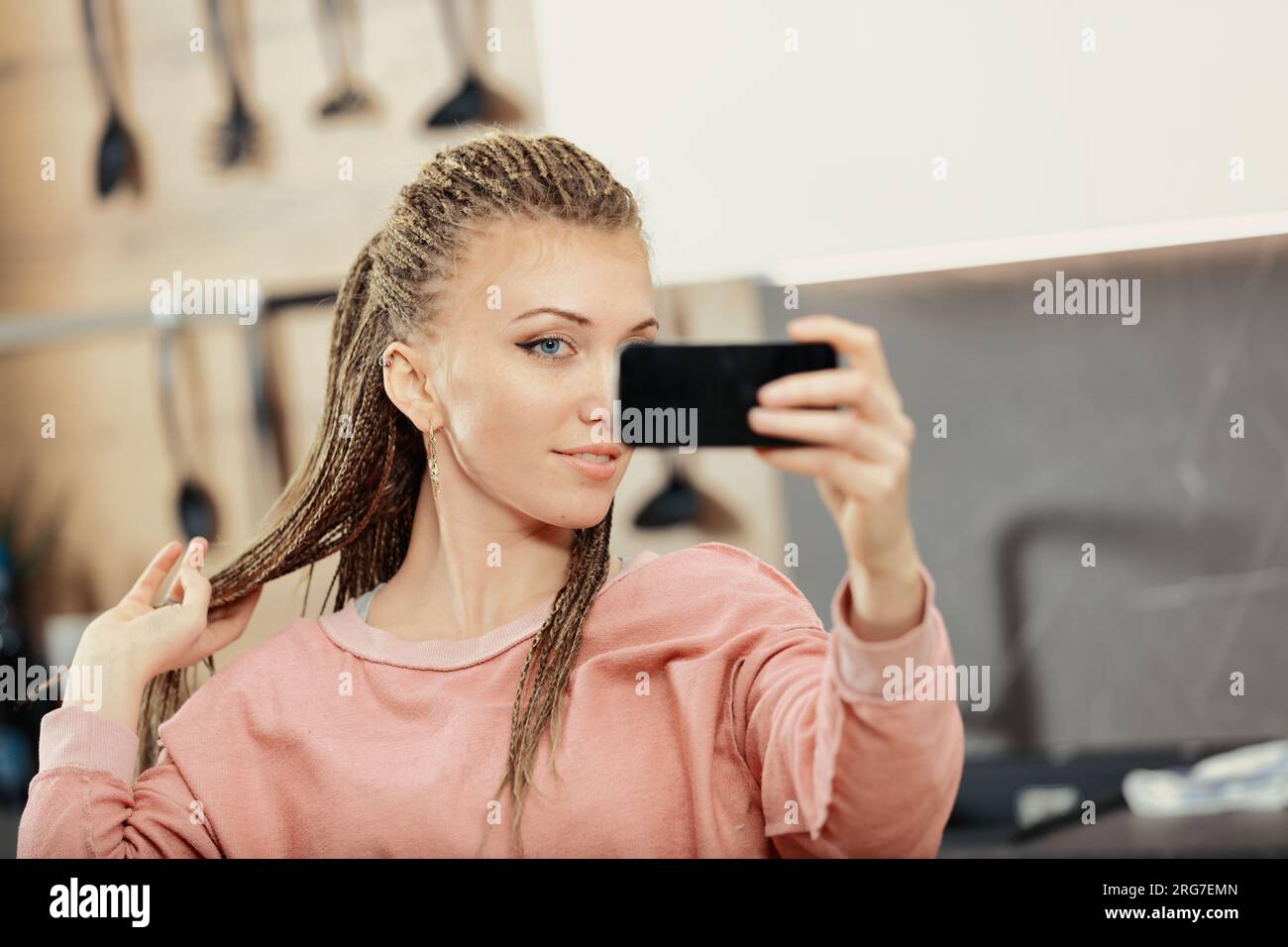 Frau mit Boxgeflechten genießt Smartphone und Laptop in der Küche für Arbeit, Lernen und Freizeit. Die Leichtigkeit sozialer Medien hat Nachteile Stockfoto