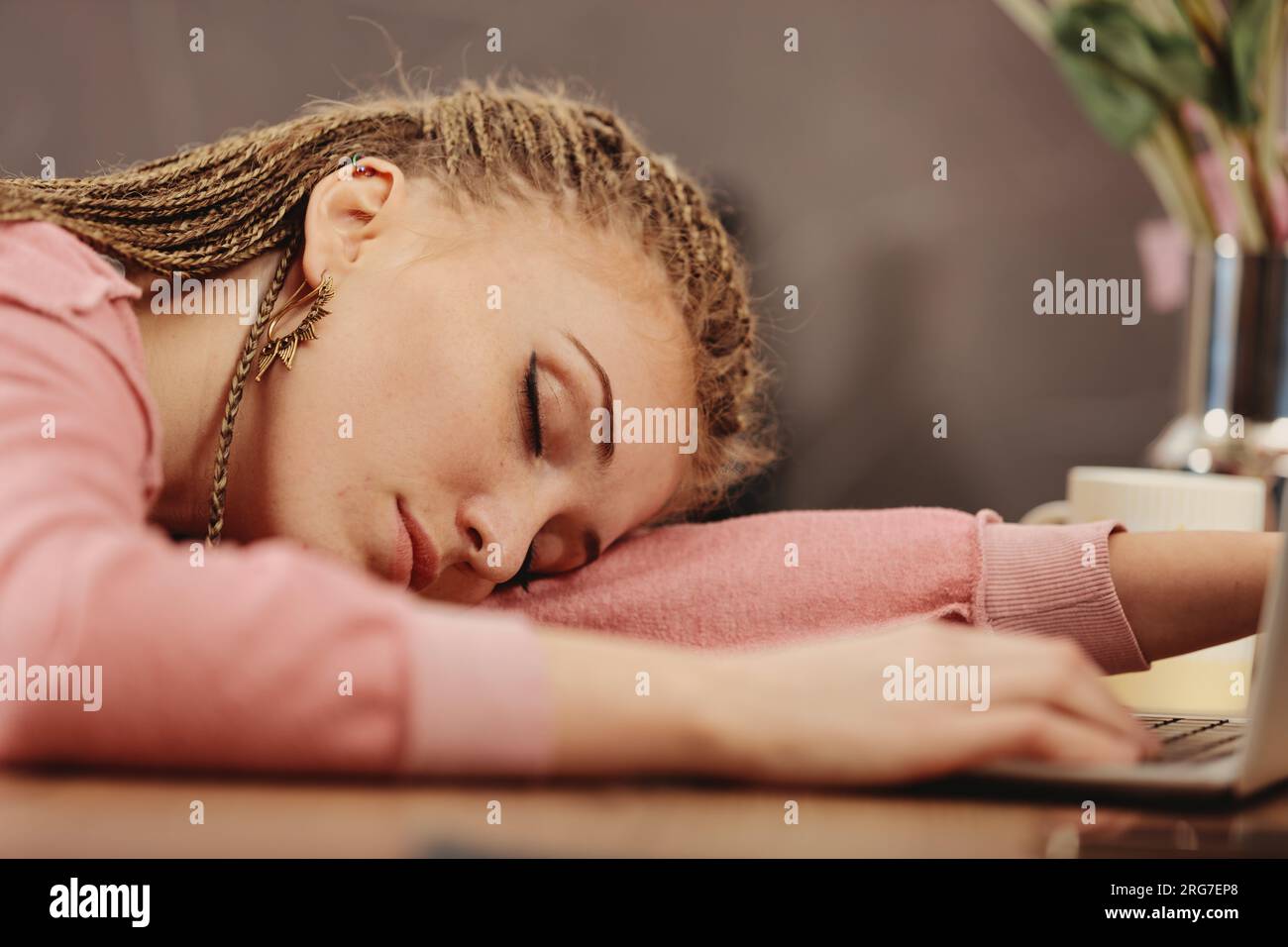 Eine junge Frau mit Boxgeflecht schläft auf der Laptop-Tastatur ein, Hand auf Handy. Erschöpft von Arbeit oder Studium Stockfoto