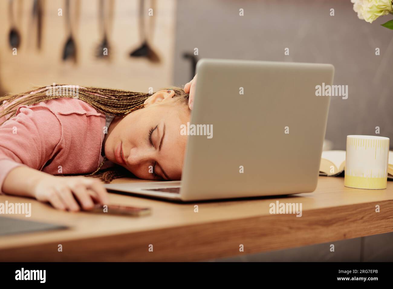 Sie schläft auf ihrem Laptop in der Küche und eine müde Frau mit Boxgeflechten ruht sich nach harter Arbeit oder nach dem Lernen aus Stockfoto