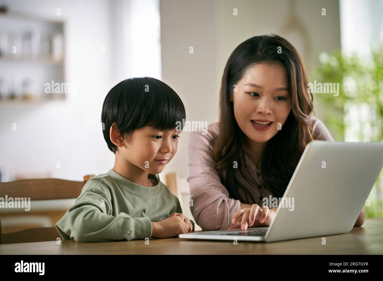 Glückliche asiatische Mutter und Sohn, die zu Hause an einem Tisch sitzen und sich einen Film mit einem Laptop anschauen Stockfoto