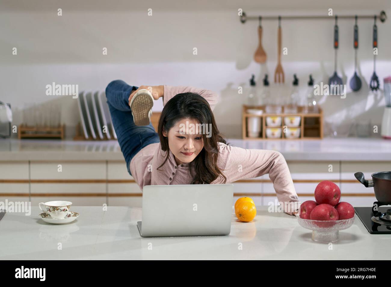 Junge asiatische Geschäftsfrau, Freiberuflerin, die sich zu Hause in der Küche mit einem Laptop die Beine vertreten kann Stockfoto