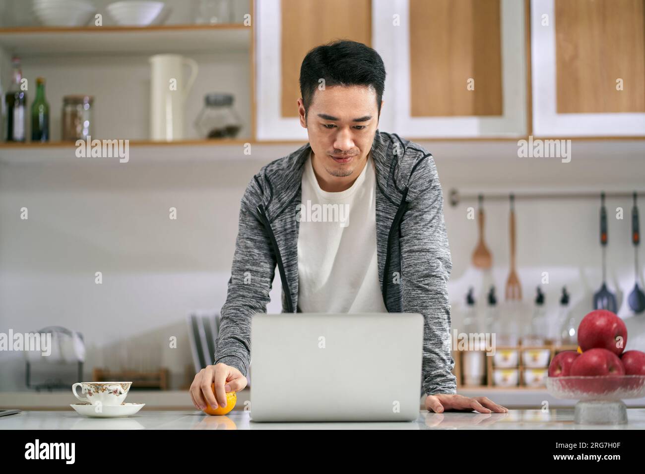 Junger asiatischer Geschäftsmann, der zu Hause in der Küche mit einem Laptop arbeitet Stockfoto
