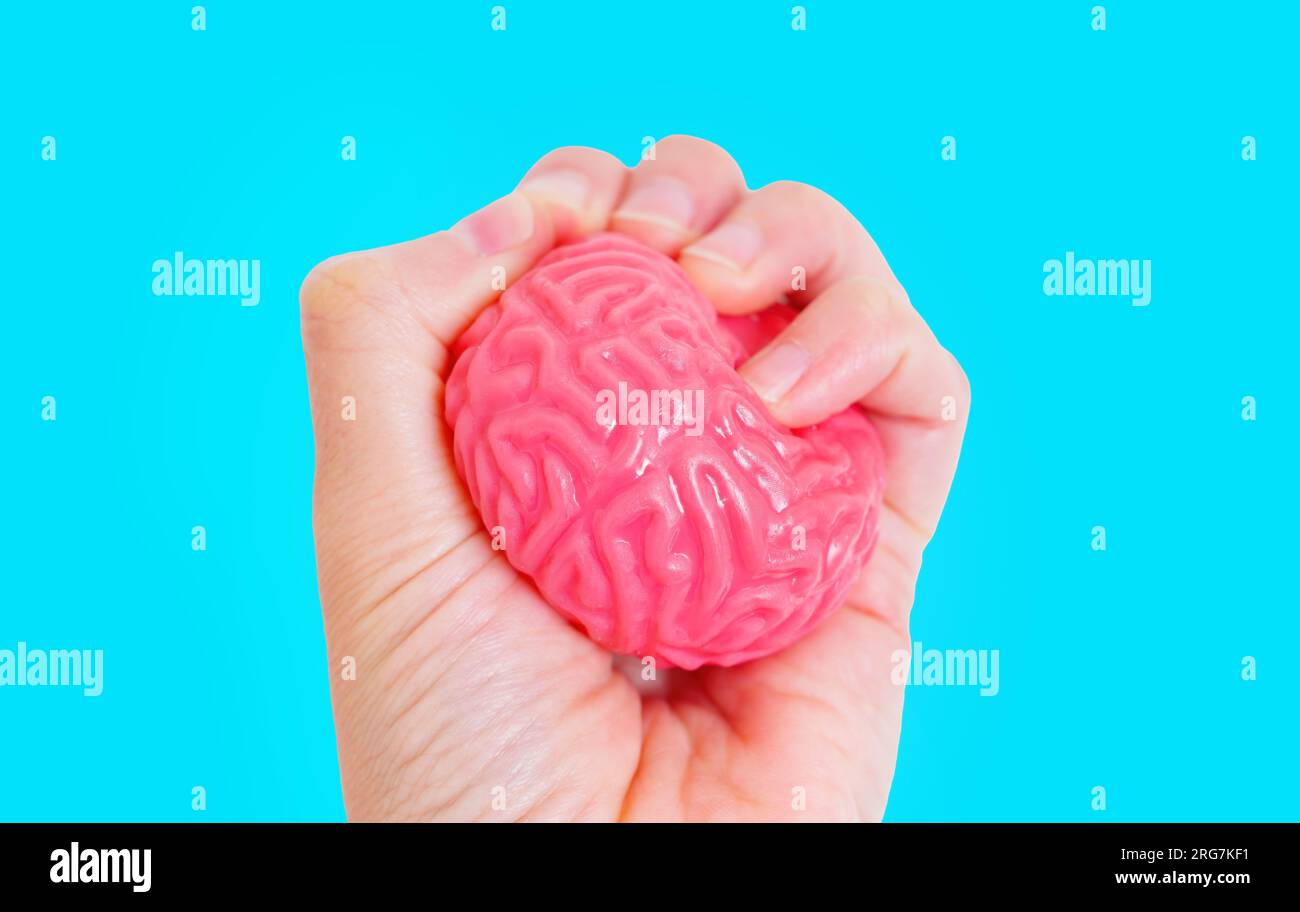 Hand drückt ein gelartiges menschliches Gehirnmodell vor blauem Hintergrund, was den Akt der Herausforderung mentaler Grenzen und des Durchbruchs kognitiver b signalisiert Stockfoto