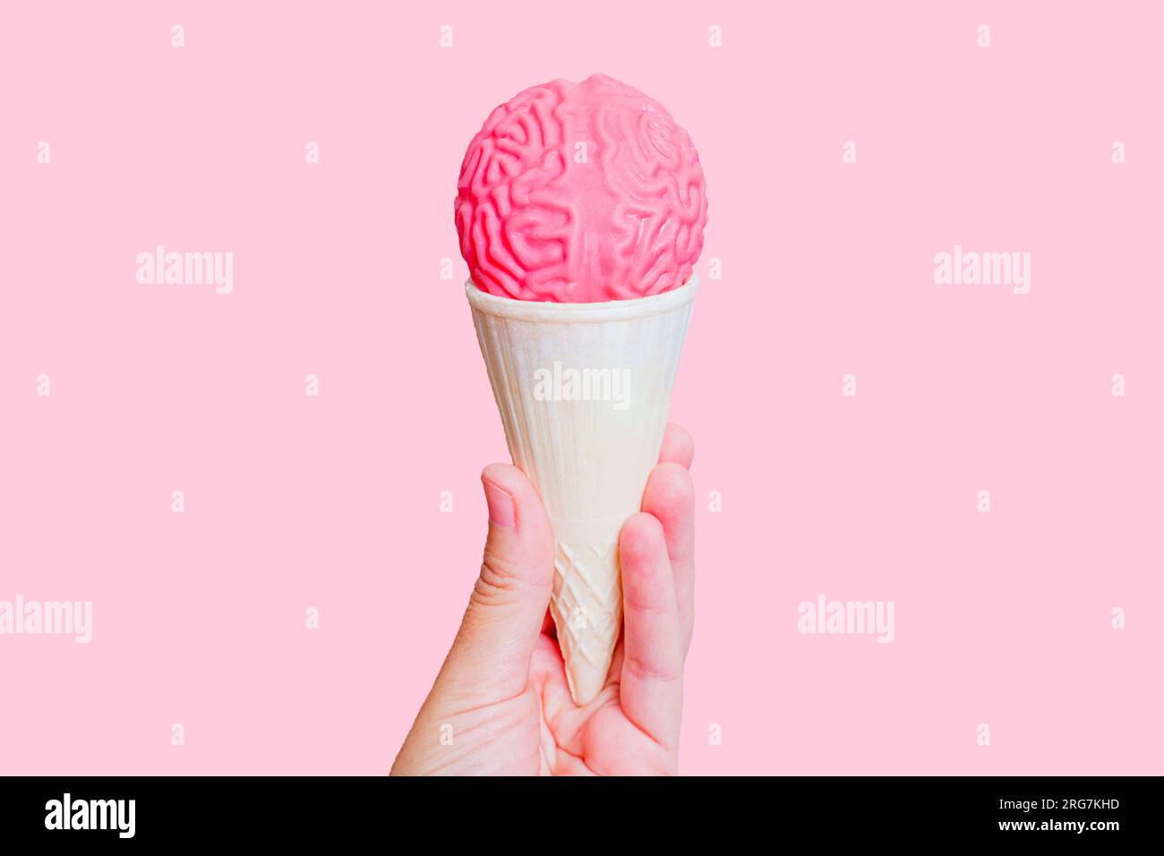 Eiskegel gekrönt mit gelee-ähnlichem menschlichem Hirnmodell in der Hand isoliert auf pinkem Hintergrund. Abenteuerkonzept mit aufmerksamer Verkostung. Stockfoto